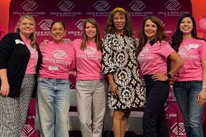 Group of people standing together indoors wearing matching pink shirts in front of a branded event backdrop.