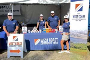 Group of people standing outdoors behind a table displaying materials and signage at a community event booth.
