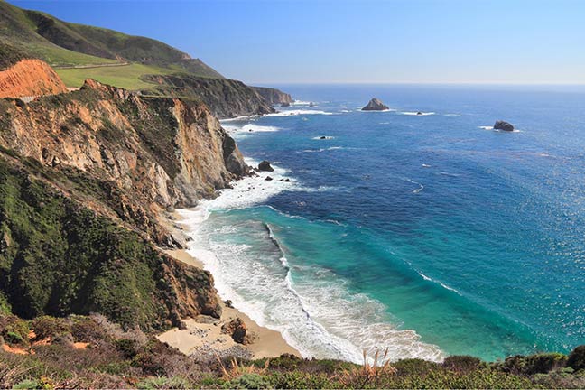 Rocky coastal cliffs rise above a narrow sandy beach.